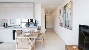 A modern kitchen with white cabinets, a dining area with wicker chairs, and a TV on a wooden stand. - A111 - Condo with amazing view (Sint Maarten)