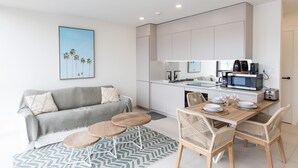 A modern kitchen with white cabinets, a microwave, and a coffee maker. There is a dining table with chairs and a sofa with cushions. - A111 - Condo with amazing view (Sint Maarten)
