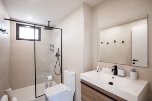 Un baño moderno con ducha de vidrio, un lavabo blanco con espejo y un inodoro.