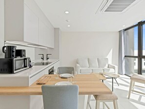 A modern kitchen with white cabinets, a built-in microwave, and a dining area with a wooden table and chairs.
