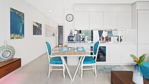 A modern kitchen with white cabinets, a built-in oven, and a coffee machine. There is a dining area with a wooden table and blue chairs. - A136 - Amazing Spacious Apartment Lagoon View with Balcony (Sint Maarten)