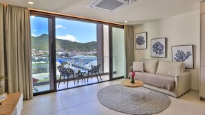 A modern living room with a large sliding glass door leading to a balcony, a beige sofa, a coffee table, and framed artwork on the wall. - A112 - Extraordinary Lagoon View with Balcony (Sint Maarten)