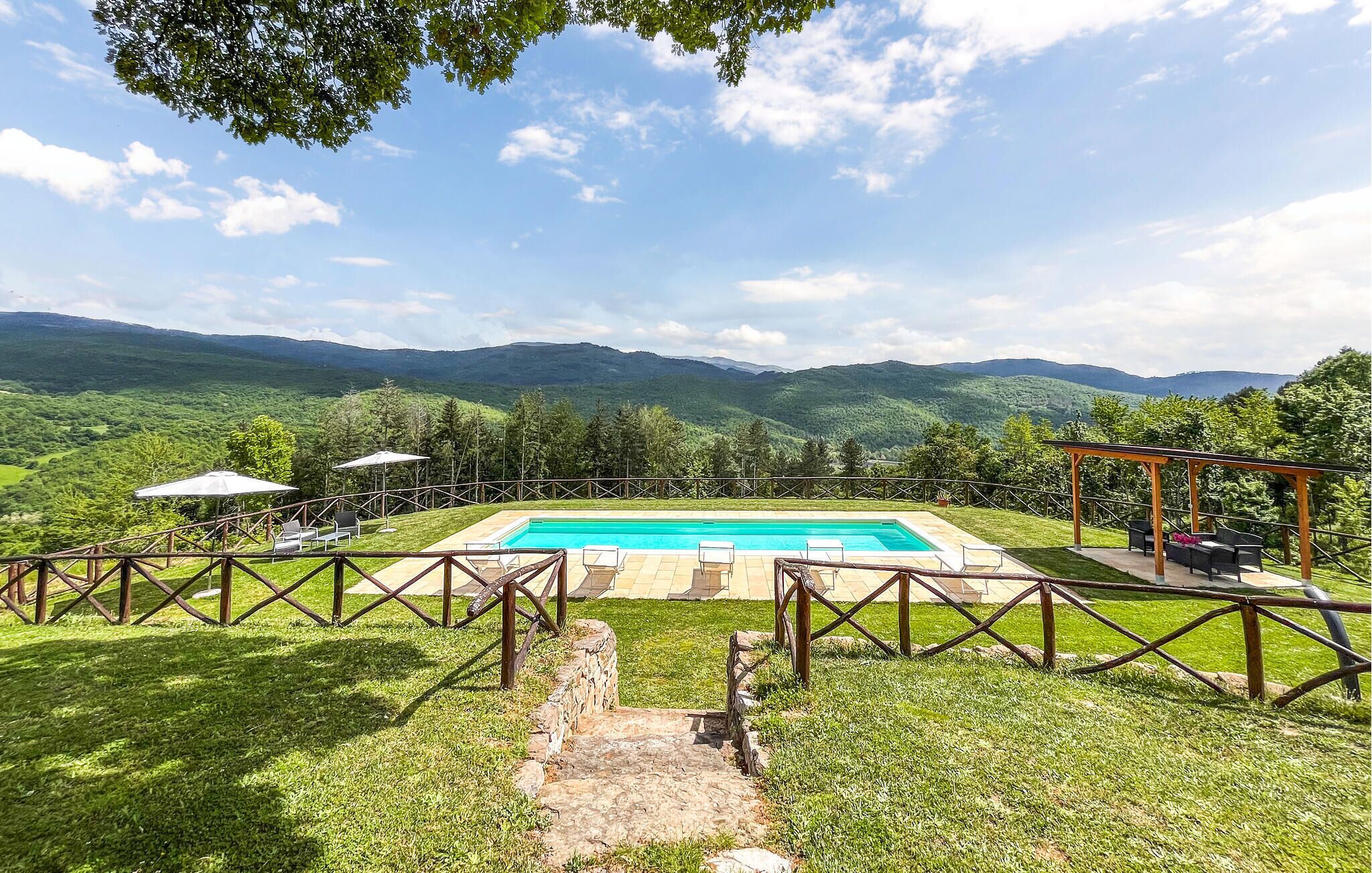 A rectangular swimming pool with a wooden deck, surrounded by a stone wall and a wooden fence.