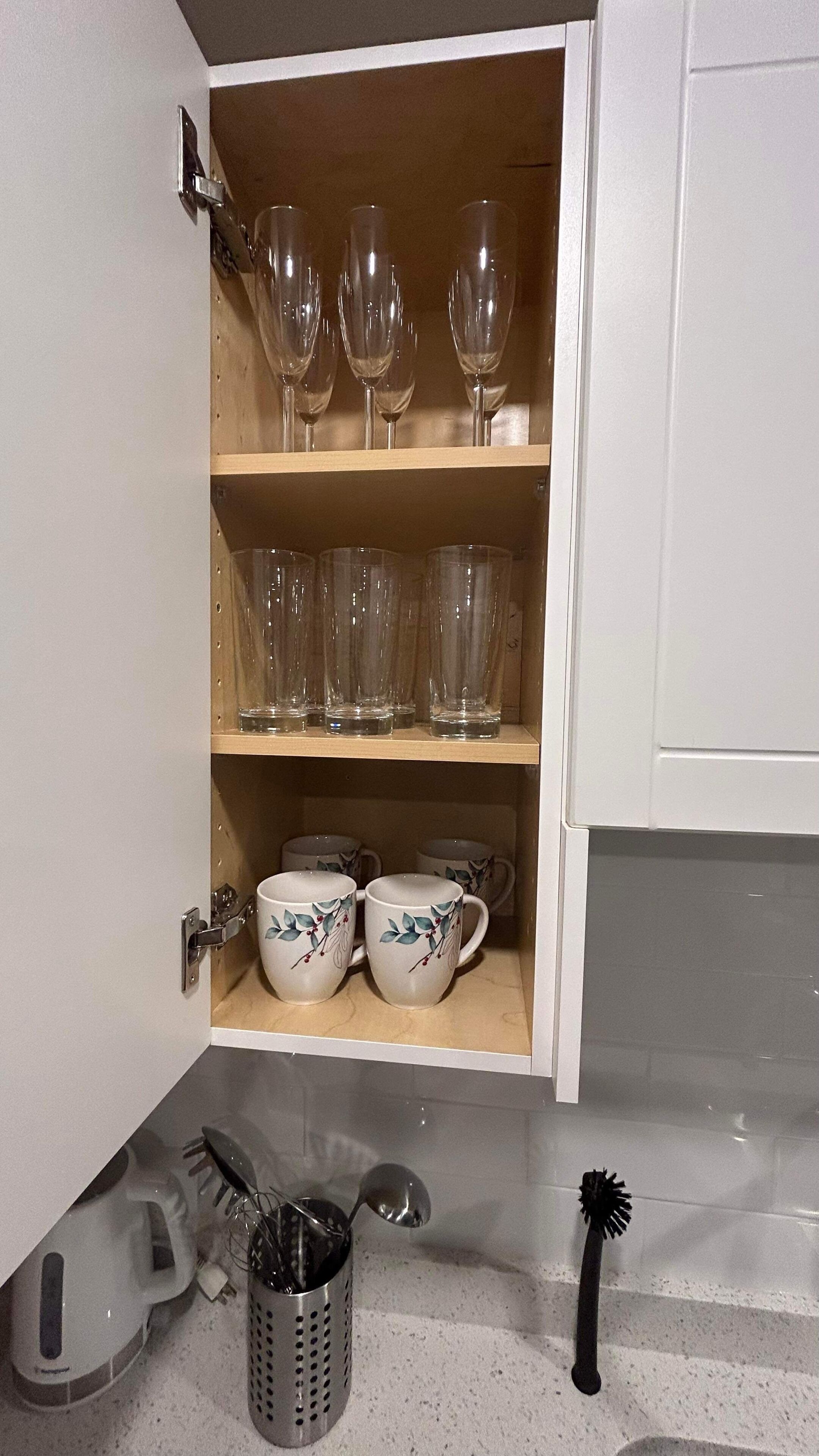 A kitchen cabinet with wine glasses and teacups.