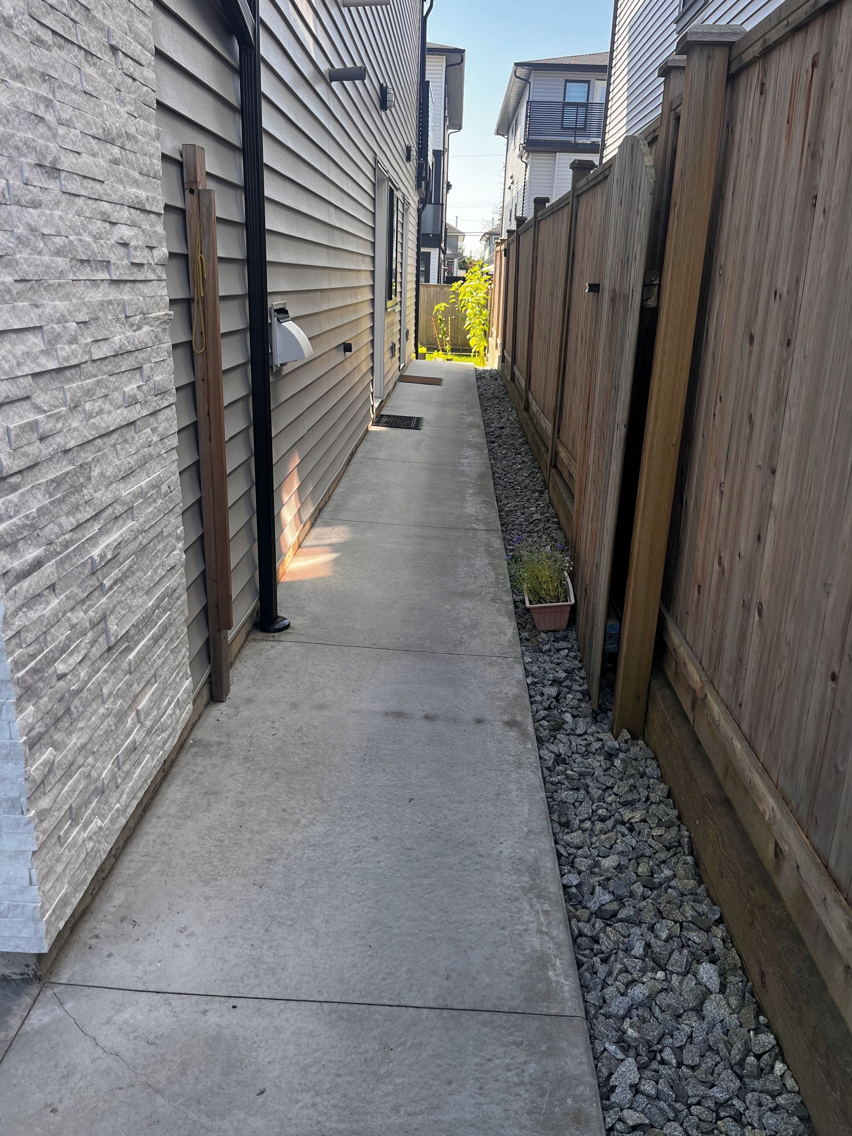 En smal gångbana av betong, med en stenmur på ena sidan och ett trästaket på den andra, som leder till ett bostadsområde.