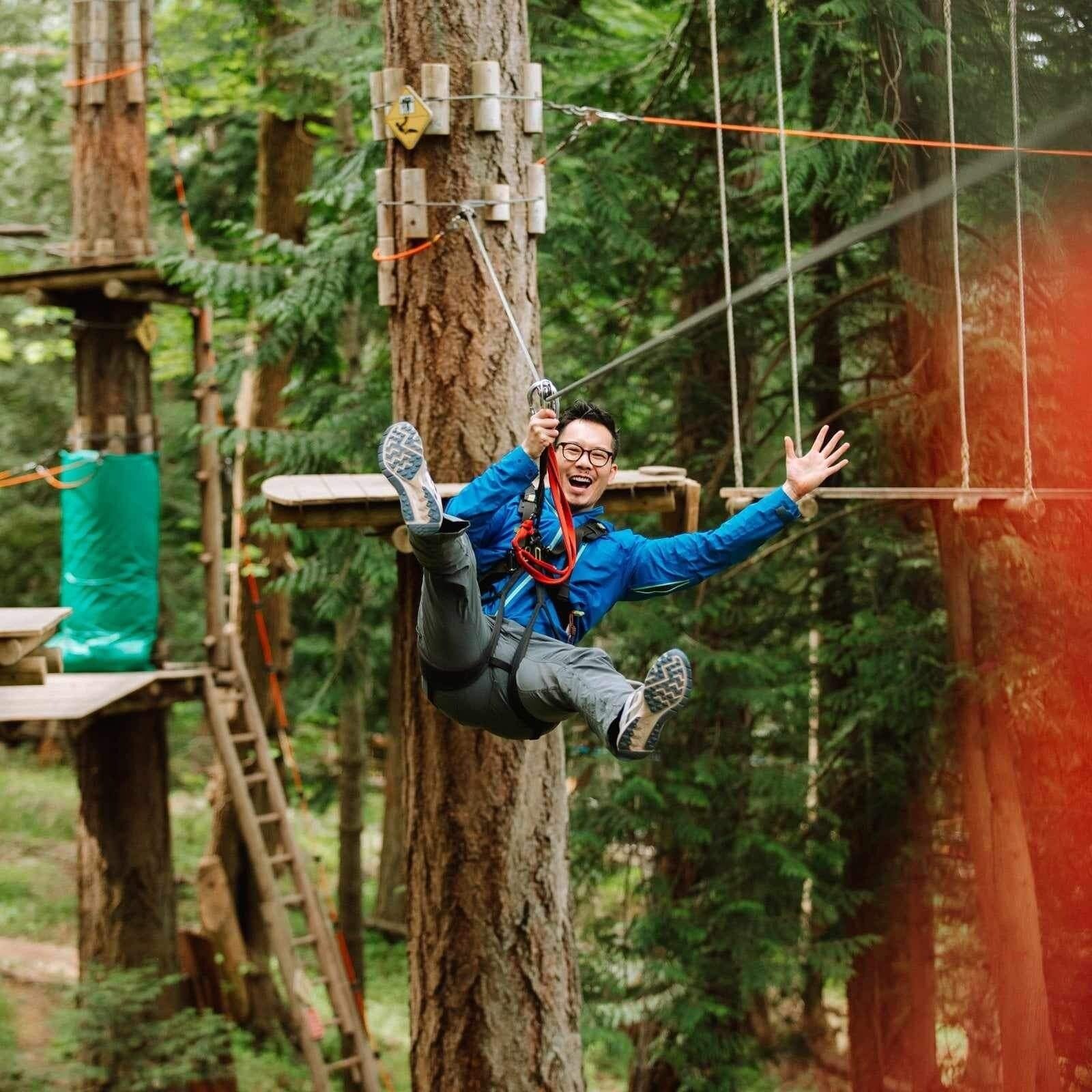 A person zip-lining through a forest with wooden platforms and ropes.