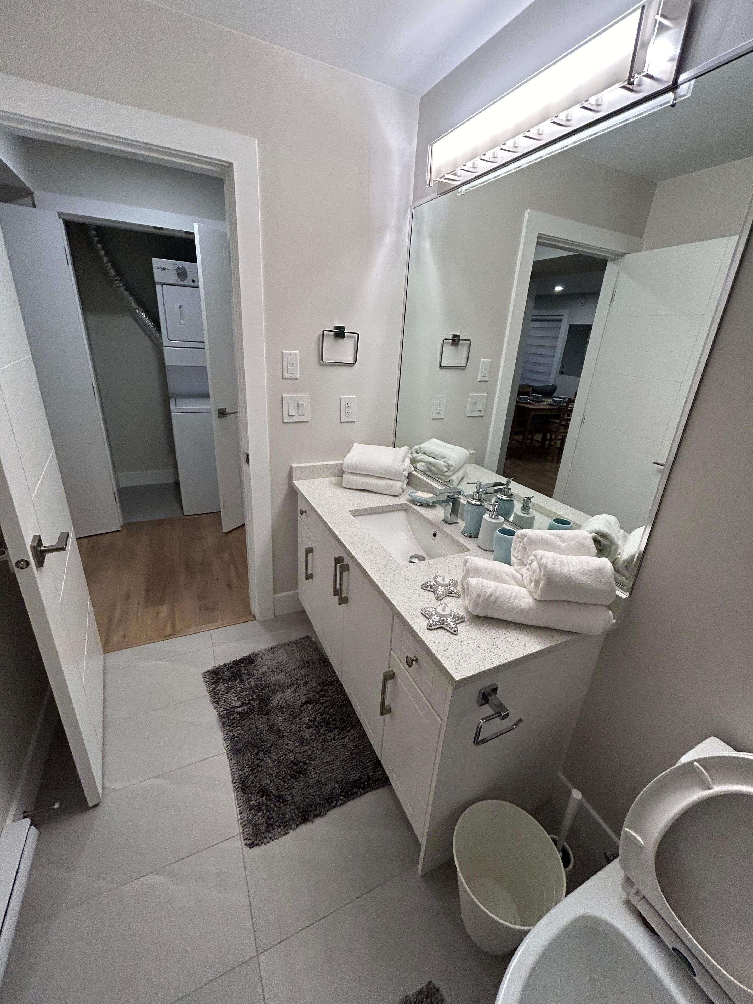 Un baño moderno con tocador blanco, un espejo grande y un inodoro.