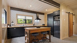 Une cuisine avec un îlot central en bois, des appareils électroménagers noirs et une fenêtre équipée de stores.