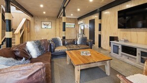 Un salon chaleureux avec un plafond en bois, des canapés en cuir, une table basse en bois et un téléviseur posé sur un meuble blanc.