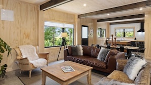 Un salon spacieux avec un canapé en cuir marron, une table basse en bois et une grande fenêtre donnant sur un paysage verdoyant.