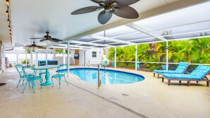 An indoor swimming pool with ceiling fans, lounge chairs, and a table with chairs.