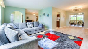 A living room with a sectional sofa, a rug, and a dining area with chairs and a table.