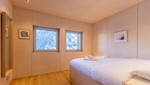 Un dormitorio con una cama grande, dos ventanas, suelo de madera y un armario de madera.