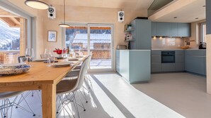 Una cocina moderna con armarios grises, una mesa de comedor de madera y vistas a una montaña nevada.