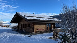 Una cabaña de madera con techo inclinado, un porche cubierto y vistas de montañas nevadas.
