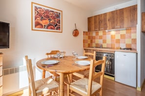Un coin repas avec une table et des chaises en bois, une cuisine avec des meubles en bois et un plan de travail carrelé, et un petit réfrigérateur.