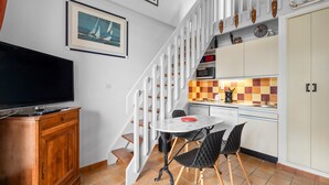 A compact living space with a TV, wooden cabinet, dining table, chairs, kitchen area, and a staircase.