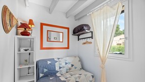 A bedroom with a bed, a shelf with a lamp, a mirror, and a window with curtains.