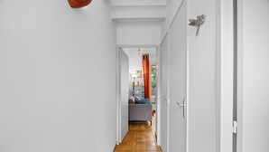 A narrow hallway with a tiled floor leading to a room with a bed and a window.