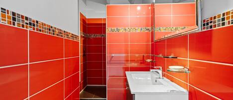 Un baño con baldosas rojas, un lavamanos blanco y un espejo.
