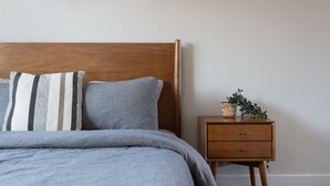 A bedroom with a wooden headboard, a grey bedspread, striped pillows, a small wooden nightstand with a plant, and a window with a view of bare trees. - Newly Built Home in Central Austin- 10 mins to downtown.  (Austin)