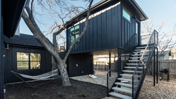 A modern two-story house with a black exterior, a tree in the yard, a hammock, and a staircase leading to the upper level. - Newly Built Home in Central Austin- 10 mins to downtown.  (Austin)