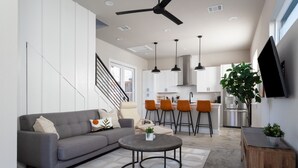 A modern living room with a grey sofa, a coffee table, and a staircase leading to an open kitchen area with bar stools and a large plant. - Newly Built Home in Central Austin- 10 mins to downtown.  (Austin)
