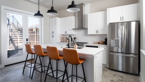 A modern kitchen with white cabinets, a stainless steel refrigerator, and a central island with bar stools. - Newly Built Home in Central Austin- 10 mins to downtown.  (Austin)