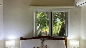 A neatly made bed with white linens, two bedside lamps, and a window with a view of greenery.