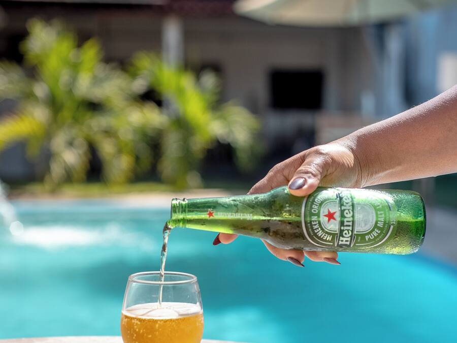 Una mano versa della birra in un bicchiere accanto a un tavolo a bordo piscina, con vista su un edificio sullo sfondo.
