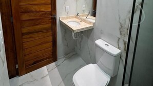 A bathroom with a wooden door, a marble sink, a toilet, and a glass shower enclosure. - Pousada Amoré (Ipojuca)