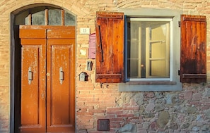 A brick building with a double wooden door and a window with shutters.