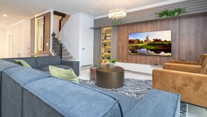 A modern living room with a large flat-screen TV, a staircase, and a cozy seating area.