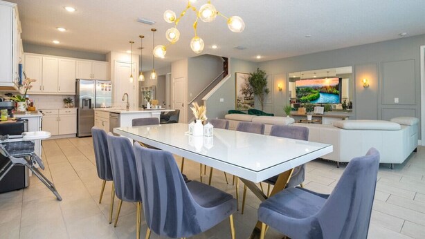 A modern kitchen with white cabinets, a stainless steel refrigerator, and a dining area with a glass table and grey chairs. - House Resort at Encore Reunion - Disney (Kissimmee)