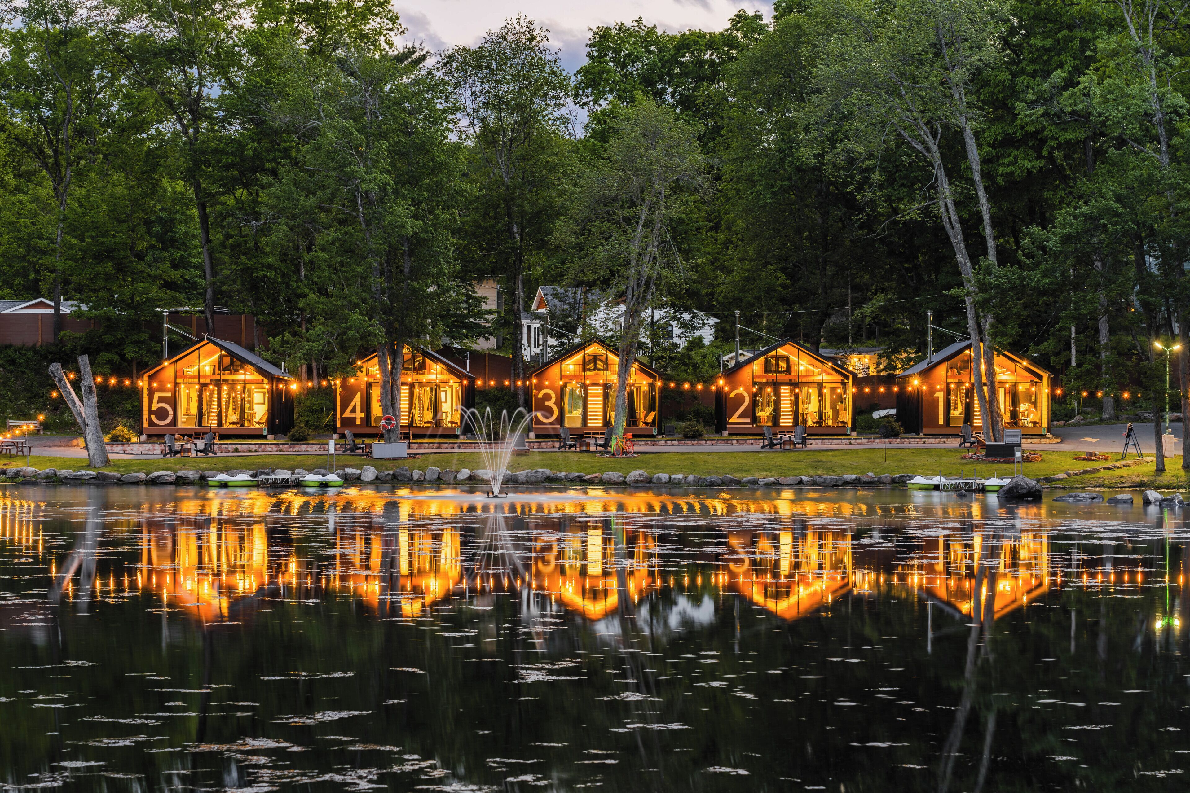 A lakeside property with numbered cabins, a fountain, and a reflection in the water.