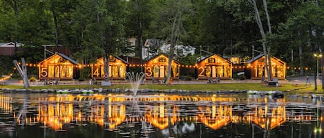 A lakeside property with numbered cabins, a fountain, and a reflection in the water.