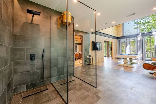 A modern interior with a glass-enclosed shower, a billiards table, and a view of the outdoors.