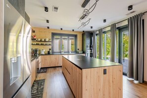 A modern kitchen with wooden cabinets, a large island, stainless steel appliances, and large windows with curtains.