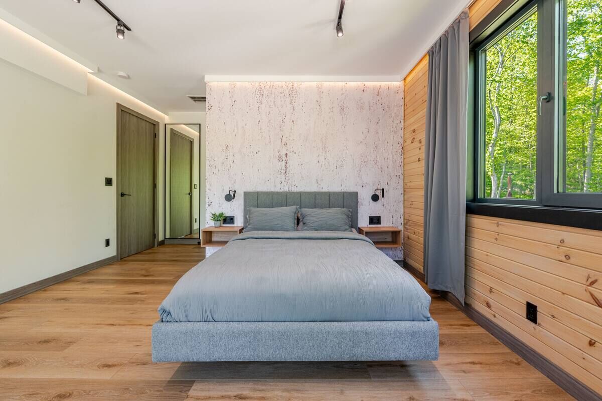 Ein modernes Schlafzimmer mit einem großen Bett, Holzpaneelen und einem Fenster mit Blick auf Bäume.