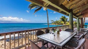 A covered outdoor dining area with a view of the ocean and a beach.
