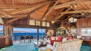 A spacious living area with a wooden ceiling, a sofa set, a coffee table, and a view of the ocean.