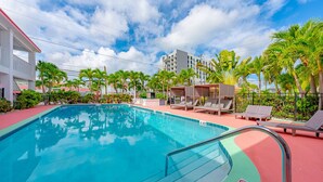 A swimming pool with lounge chairs and palm trees, surrounded by buildings.