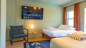 Ein Hotelzimmer mit Bett, einem Sessel, einem an der Wand montierten Fernseher und einem Fenster mit Vorhängen.