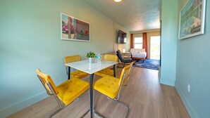 Ein Essbereich mit einem weißen Tisch und gelben Stühlen, einem Fernseher an der Wand und einem Gemälde über dem Tisch.