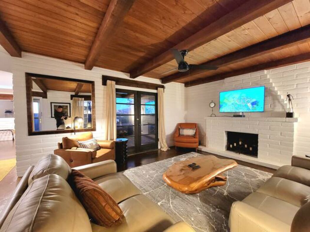 A modern living room with a wooden ceiling, a fireplace, a television, and leather sofas.