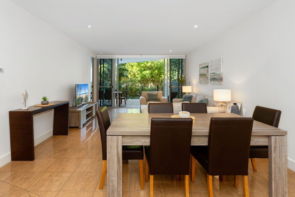 A modern dining area with a wooden table and chairs, a kitchen counter, and a view of the outdoors.