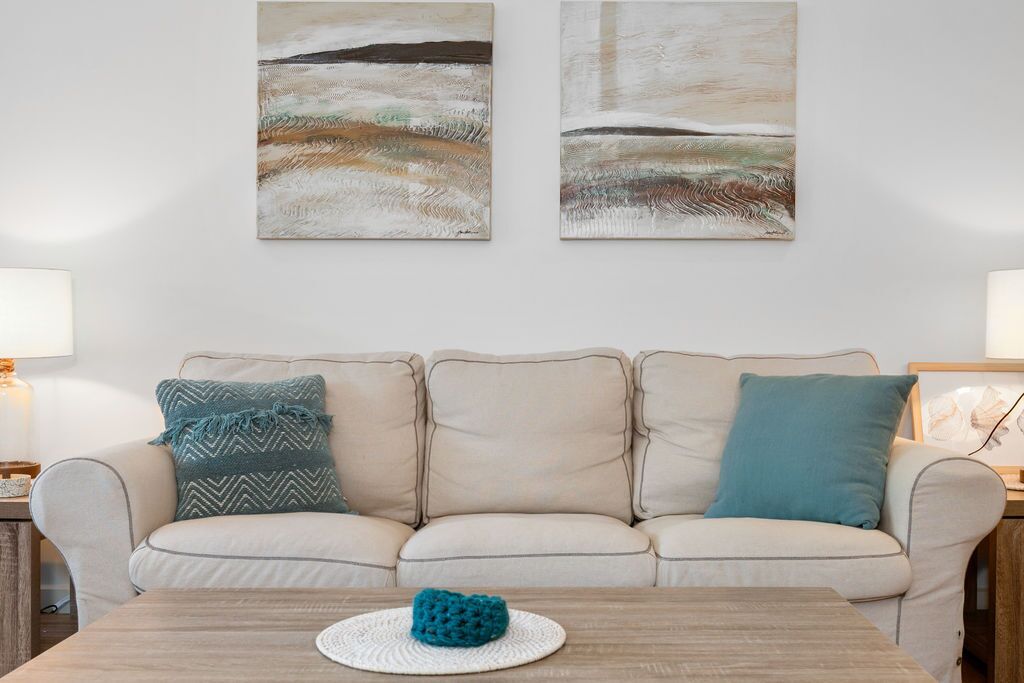 A neutral-toned living room with a beige sofa, two pillows, a round coffee table, and abstract wall art.