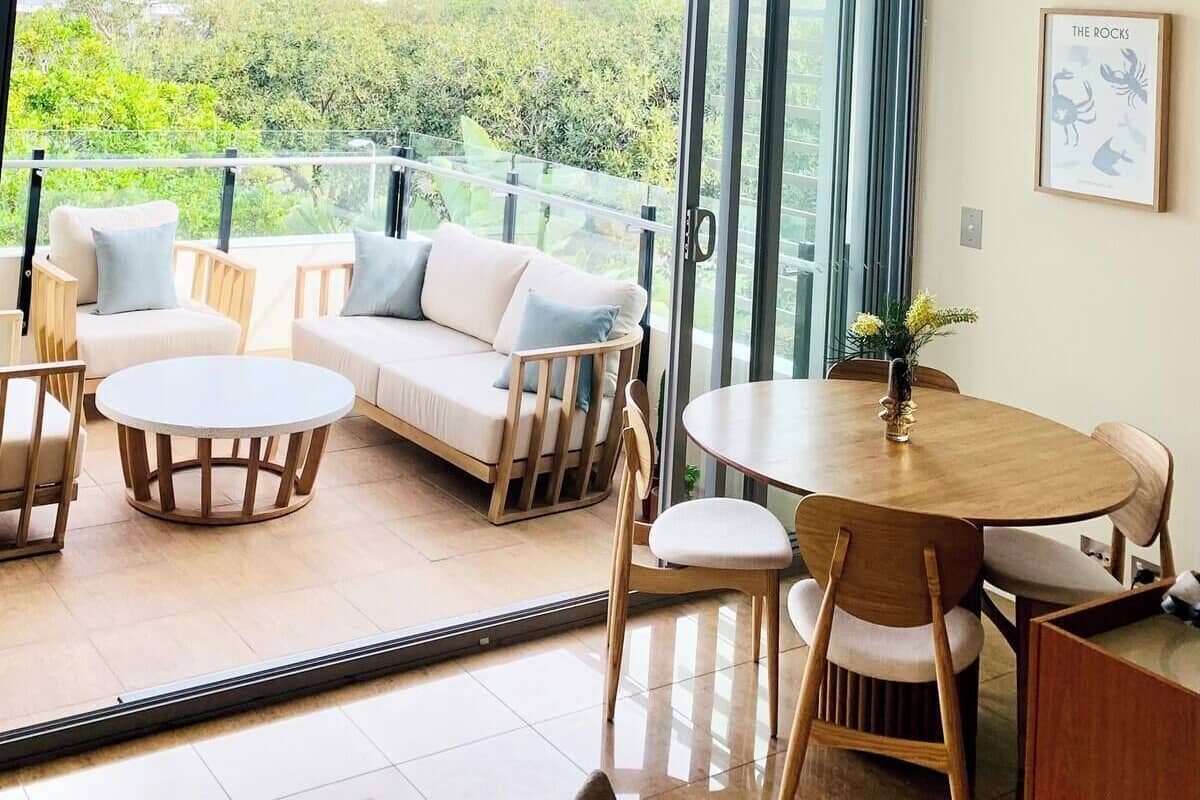 Un salon moderne comprenant un canapé, des fauteuils, une table ronde et un balcon offrant une vue sur la verdure et les montagnes.