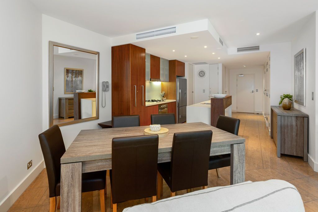 Eine moderne Küche mit Holzschränken, einem Esstisch mit Stühlen und einem sichtbaren Kühlschrank.