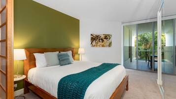 Une chambre d’hôtel moderne avec un grand lit, un mur d’accent vert, un tableau et une porte-fenêtre coulissante donnant sur un balcon.